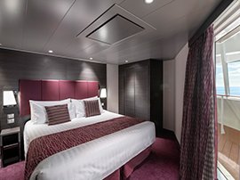Luxurious cruise ship cabin with a large bed, vibrant decor, and balcony overlooking the ocean | MSC Cruises Luxurious cruise ship cabin with a large bed, vibrant decor, and balcony overlooking the ocean | MSC Cruises