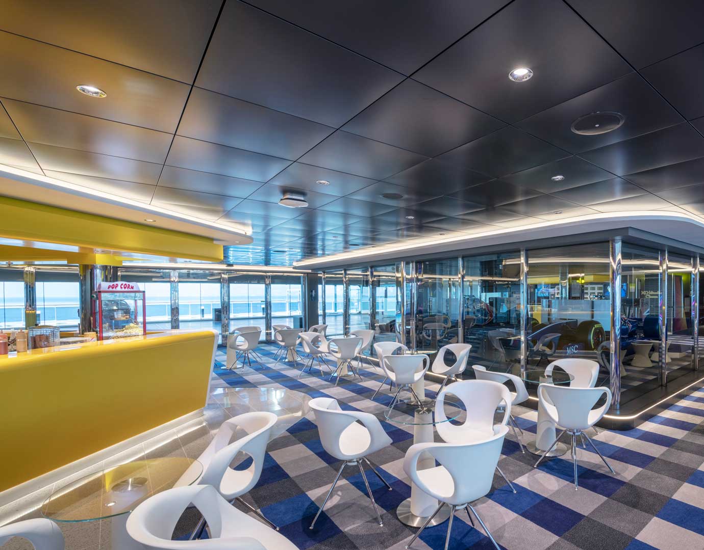 Modern onboard café with sleek white chairs, yellow counter, and ocean views | MSC Cruises Modern onboard café with sleek white chairs, yellow counter, and ocean views | MSC Cruises