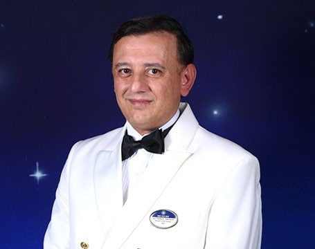 Crew member in a white formal uniform with an MSC name badge against a starry backdrop | MSC Cruises Crew member in a white formal uniform with an MSC name badge against a starry backdrop | MSC Cruises