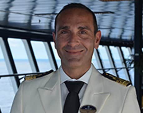 A captain in a white uniform aboard a cruise ship with ocean views | MSC Cruises A captain in a white uniform aboard a cruise ship with ocean views | MSC Cruises