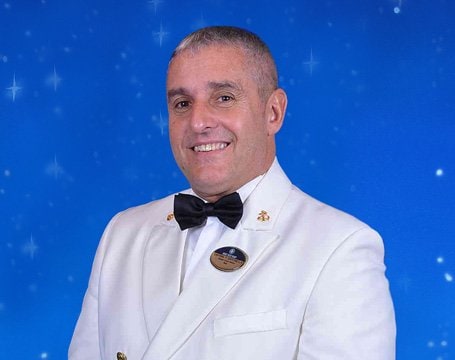 Crew member in formal white uniform with a bow tie against a starry blue background | MSC Cruises Crew member in formal white uniform with a bow tie against a starry blue background | MSC Cruises