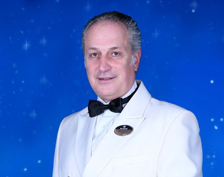 A crew member in a white uniform against a starry blue background | MSC Cruises A crew member in a white uniform against a starry blue background | MSC Cruises
