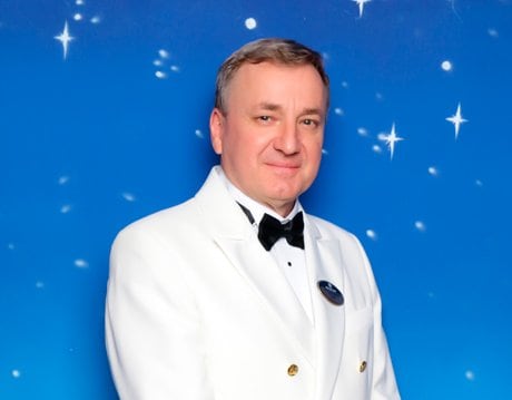 A cruise ship captain in a white uniform against a starry blue backdrop | MSC Cruises A cruise ship captain in a white uniform against a starry blue backdrop | MSC Cruises